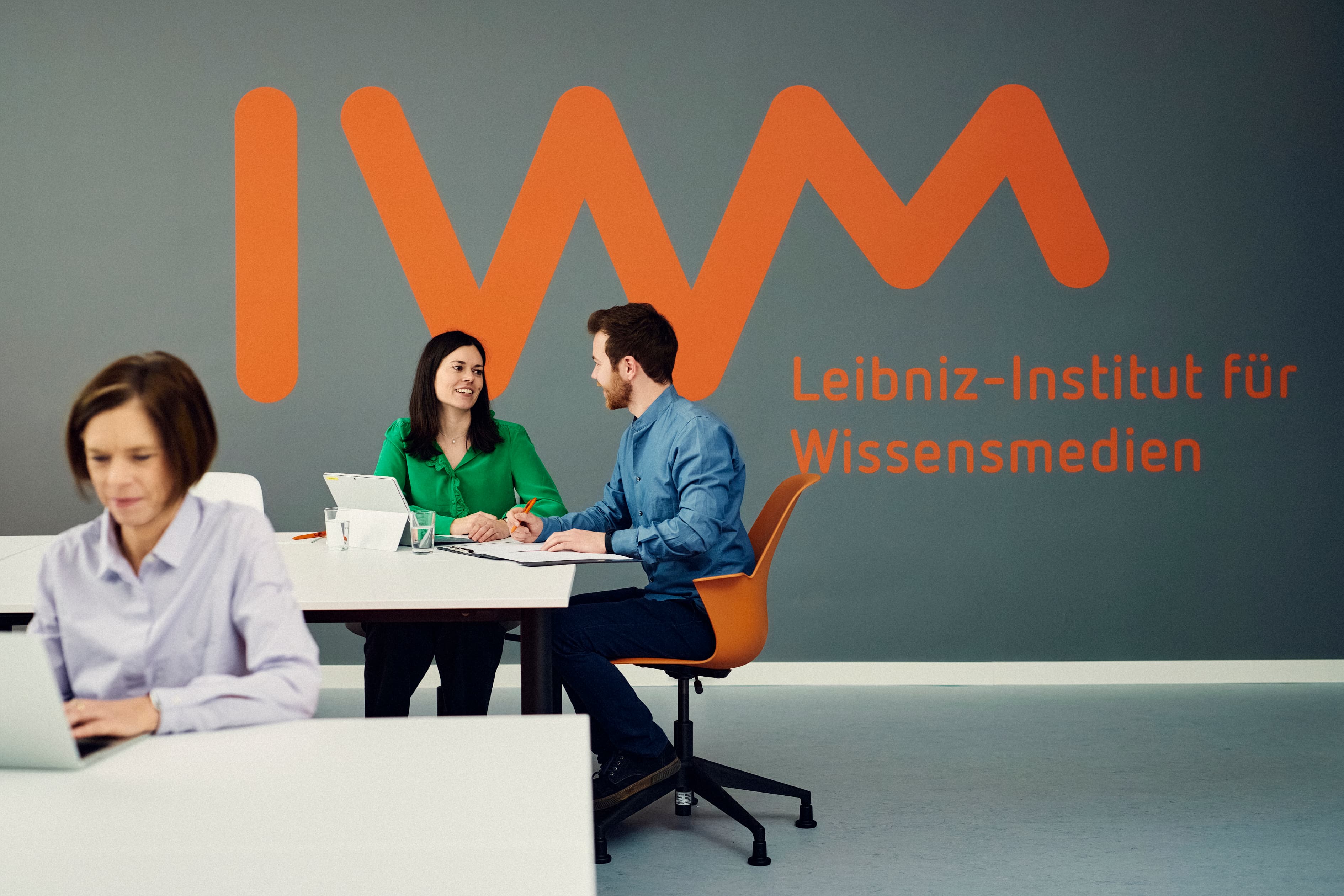 Three IWM employees work in front of a large IWM logo in the background