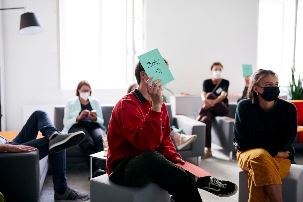IWM employees sitting together and one person holding a piece of paper labelled ‘Bot/KI’