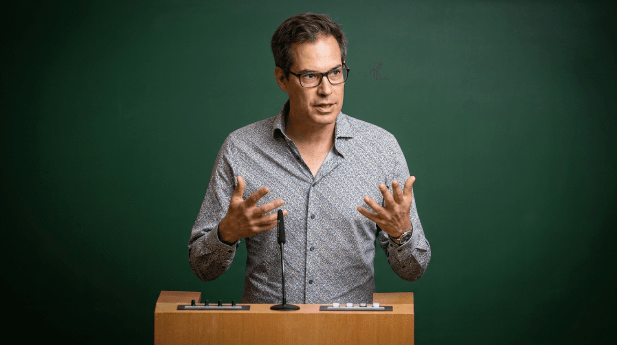 Prof. Dr. Markus Huff spricht gestikulierend an einem Rednerpult vor grünem Hintergrund