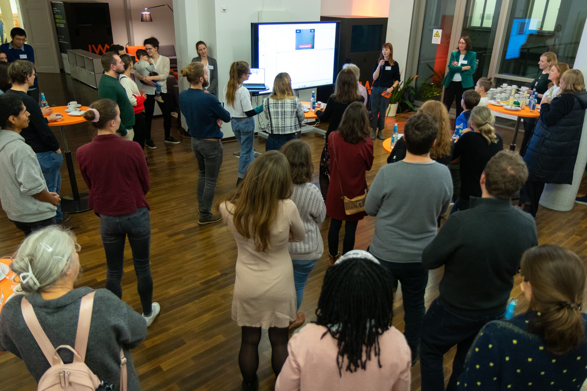 IWM alumni standing in a room and listening to an IWM employee