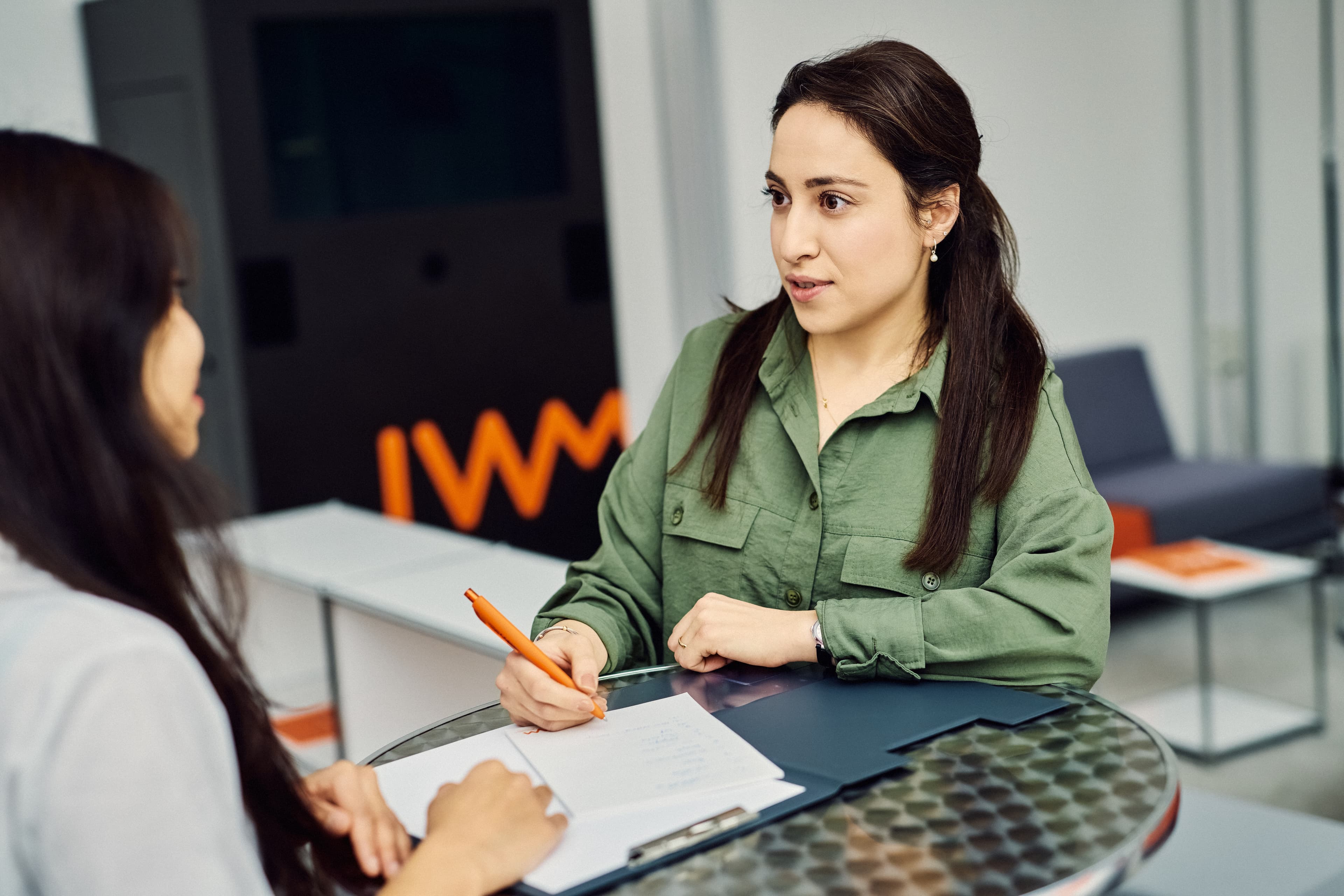 Two IWM employees are talking at a high table and taking notes